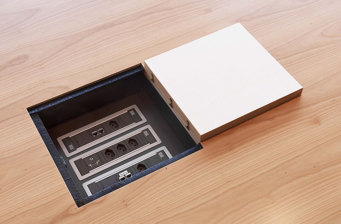 Eine Elektrifizierungsbox mit offener Klappe in einem YPSILON Holztisch.