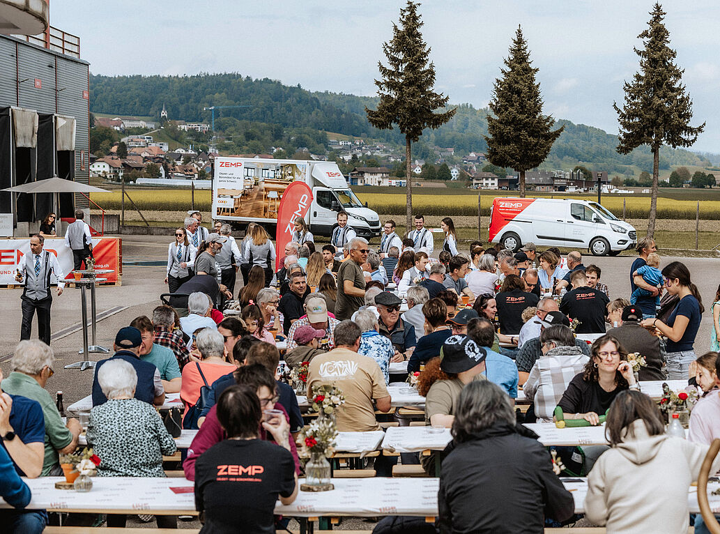 Mehrere Festbänke gefüllt mit Personen am Tag der offenen Tür bei der Zemp AG.
